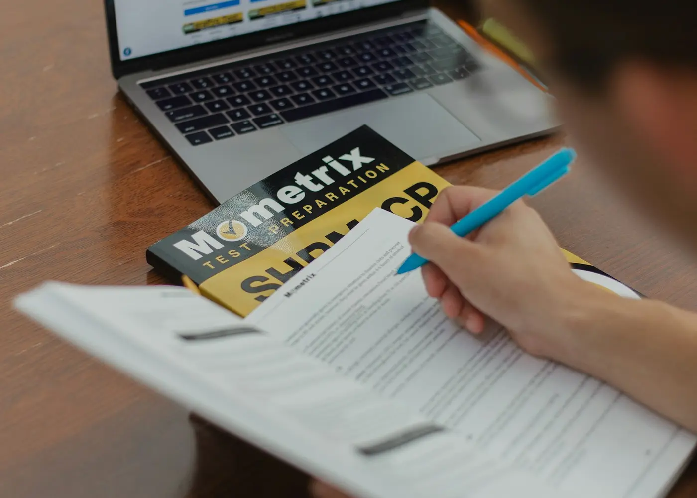 Learner writing notes beside a laptop